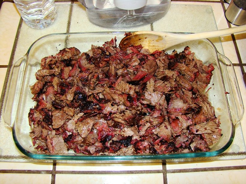 Glass baking dish filled with shredded smoked meat, with a wooden spoon resting on top