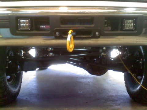 1996 Ford Bronco - Close-up view of a modified truck's rear suspension and undercarriage, a yellow tow hook and auxiliary lights.