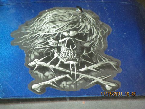 1985 Ford F-150 - A sticker of a skull with long hair and crossbones is applied to a blue surface, with a date stamp visible in the corner.