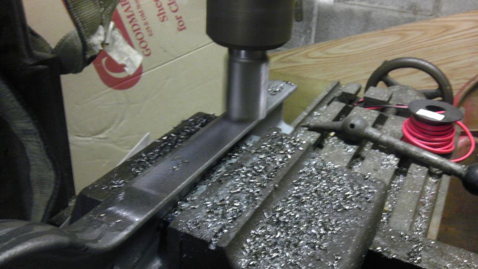 Milling machine cutting a metal part, with metal shavings on the table. A box with 'GOODMARK' is in the background