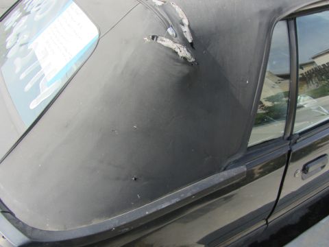 1985 Ford Mustang - The convertible top of a 1985 Ford Mustang shows significant wear and tear, with visible damage and some text on the rear window.