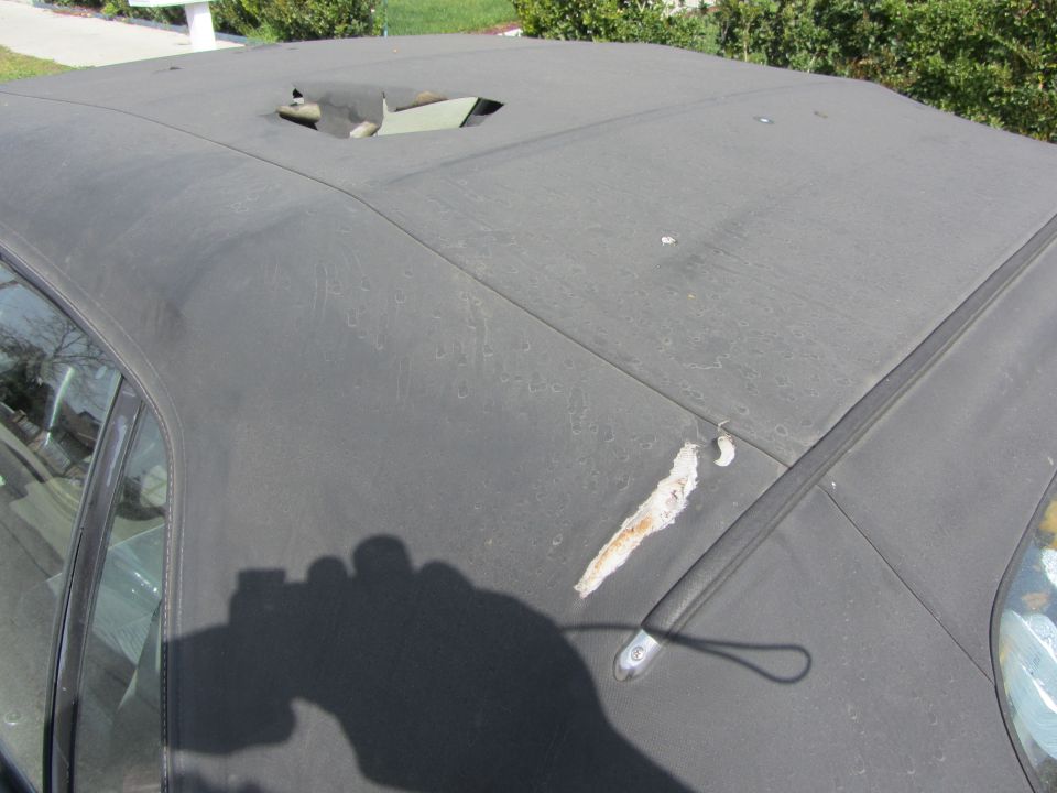 Torn black convertible top with a hole and ripped fabric near the rear