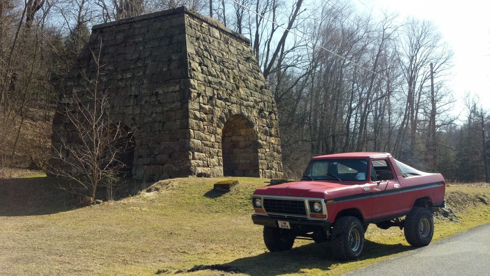 Red pickup truck with lifted suspension parked on a dirt road next to a stone structure