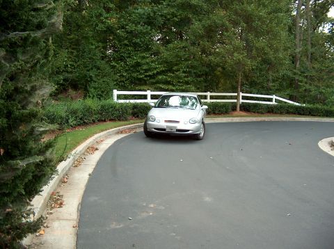 1998 Ford Taurus - This silver coupe is parked on a paved driveway with trees and a white fence in the background.