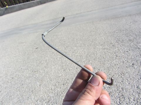 1964 Ford Ranchero - A metal rod with a hook is held in a hand against a paved surface.
