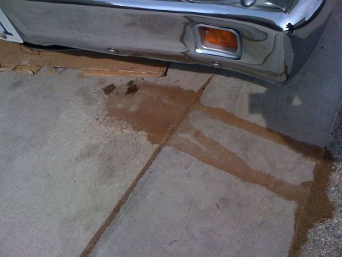 1964 Ford Ranchero - A vehicle's front bumper is visible above a puddle of brown fluid on a concrete surface.