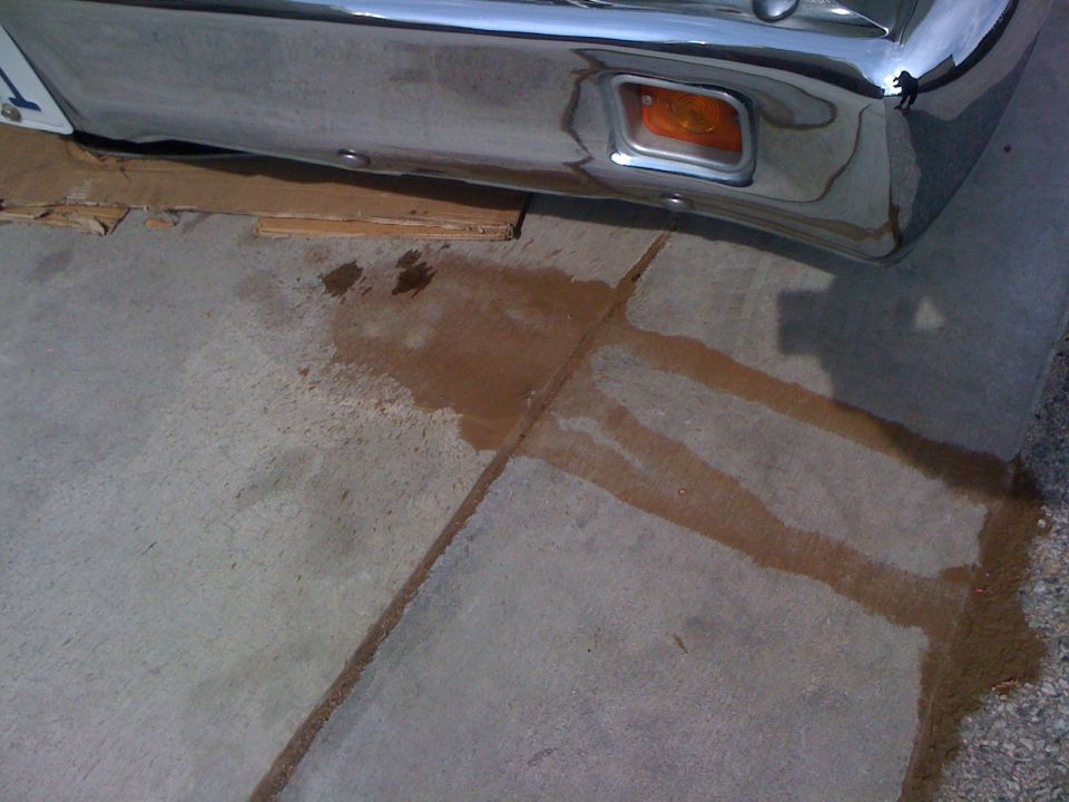 Chrome bumper with amber turn signal, sitting over cardboard with fluid stains on concrete