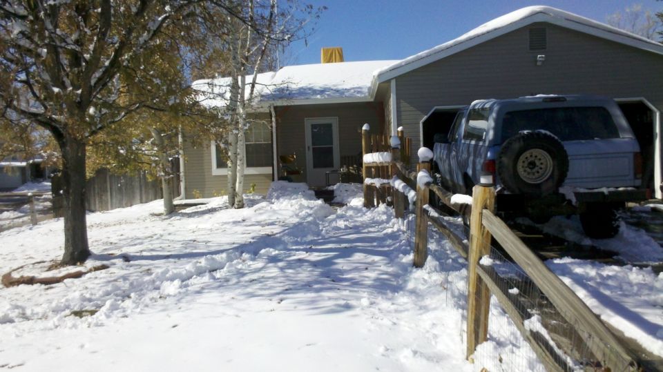 Blue Ford Bronco SUV parked under carport beside snowy house behind wood fence