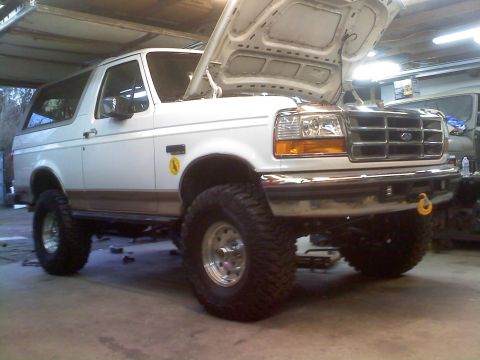 1996 Ford Bronco - White 1996 Ford Bronco lifted with large tires, hood open in a garage.