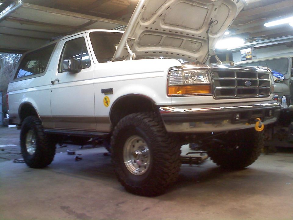 1996 Ford Bronco lifted with large tires, hood open in a garage