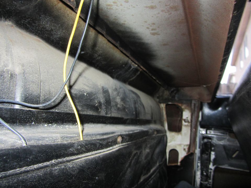Close-up of dusty interior paneling and wiring in a vehicle. Shows black textured material and exposed metal