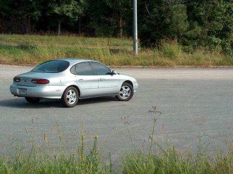 1998 Ford Taurus - A silver sedan is parked on a paved surface with vegetation and trees in the background.