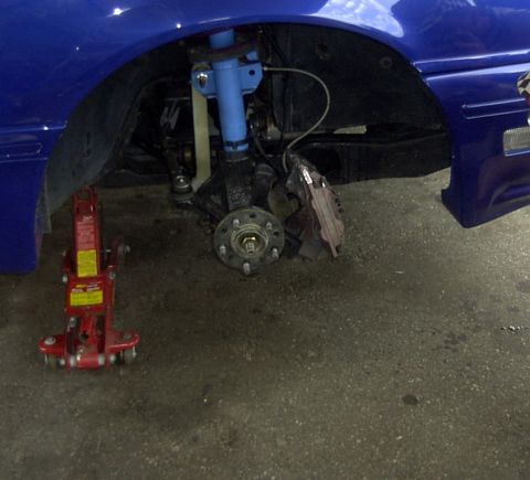 1997 Ford Taurus - Front suspension and brake assembly of a blue car, supported by a red hydraulic jack.