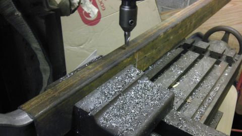 1987 Ford Ranger - A milling machine is used to drill a hole in a metal bar, with metal shavings scattered around the workpiece.