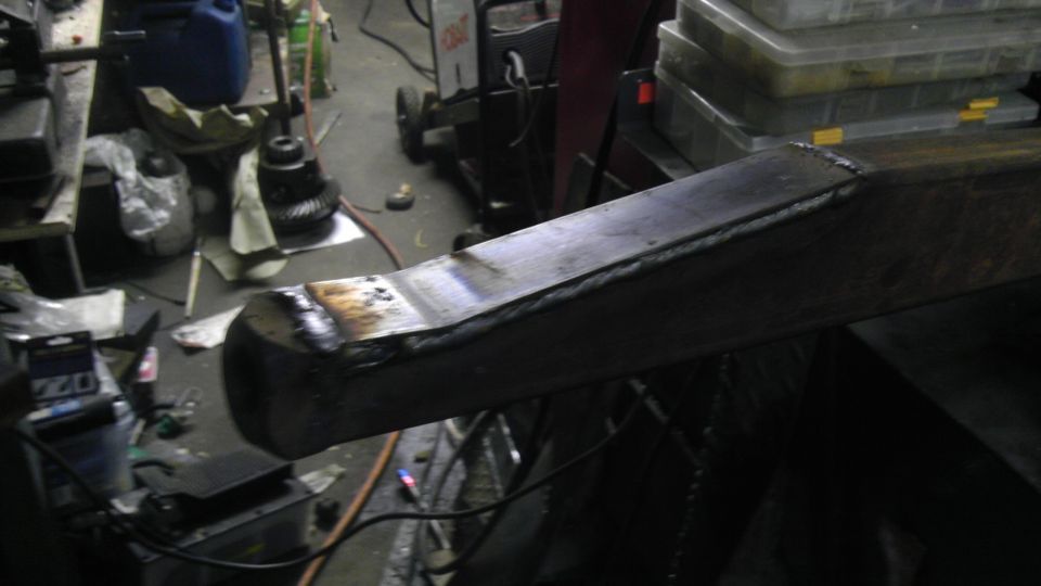 Welded metal beam with visible weld marks and a rounded end, angled view