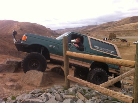 1989 Ford Bronco - A man drives a lifted Ford Bronco over large rocks on an off-road trail.