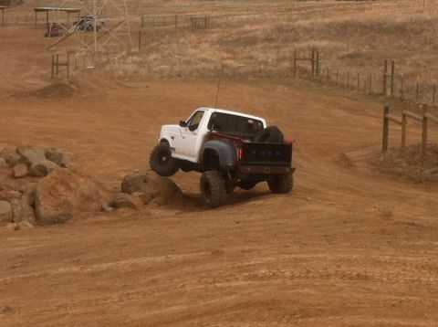 1989 Ford Bronco - White Ford Bronco with a red bed navigates a rocky off-road course.