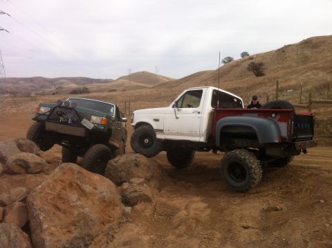 1989 Ford Bronco - Two modified trucks navigate a rocky obstacle course.