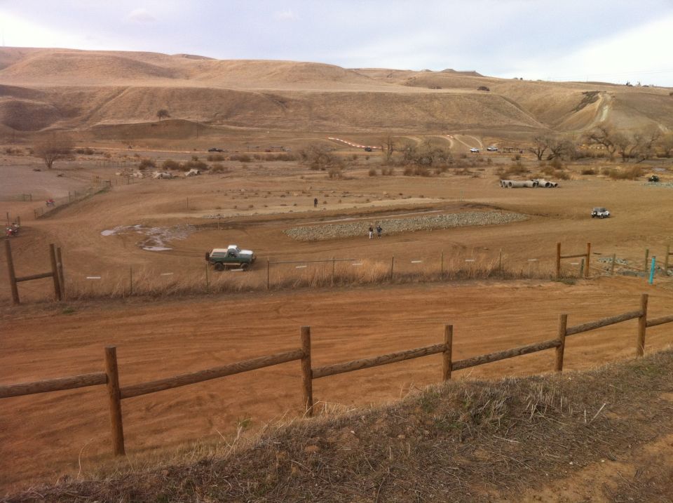 Pickup truck driving on a dirt road in a wide, open, dry landscape with hills in the background