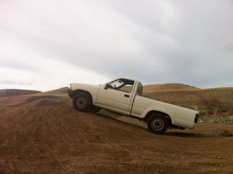 1989 Ford Bronco - A white pickup truck navigates a dirt incline under an overcast sky.