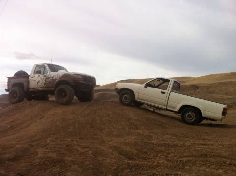 1989 Ford Bronco - Two trucks navigate challenging terrain on a cloudy day, their off-road capabilities.