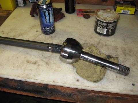 1993 Toyota 4Runner - A CV axle shaft rests on a rag next to a Monster Energy drink and a can of grease on a workbench.