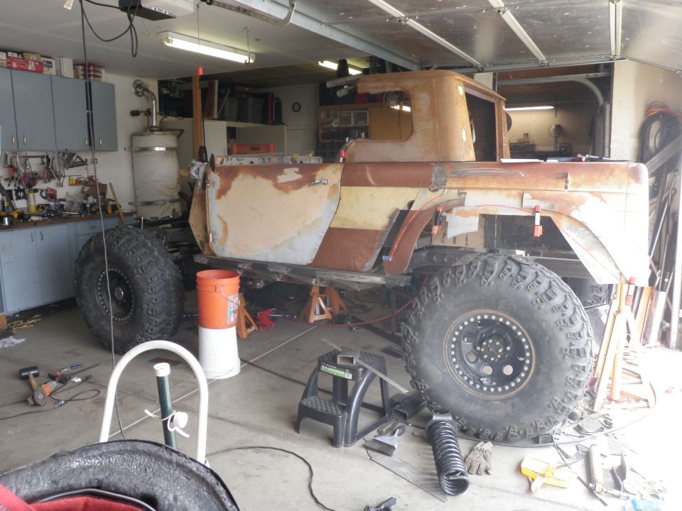Rusted pickup truck body with large off-road tires in a garage, undergoing modifications