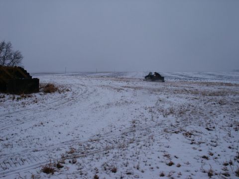 1971 Arctic Cat Panther 440 2-Pass - A snowmobile is seen traversing a snow-covered field, with a dilapidated stone building to the left.