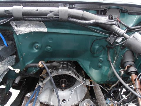 1990 Ford Bronco - Engine bay of a green Ford Bronco with the engine removed, showing the dark green firewall and inner fenders, exposed transmission bellhous…