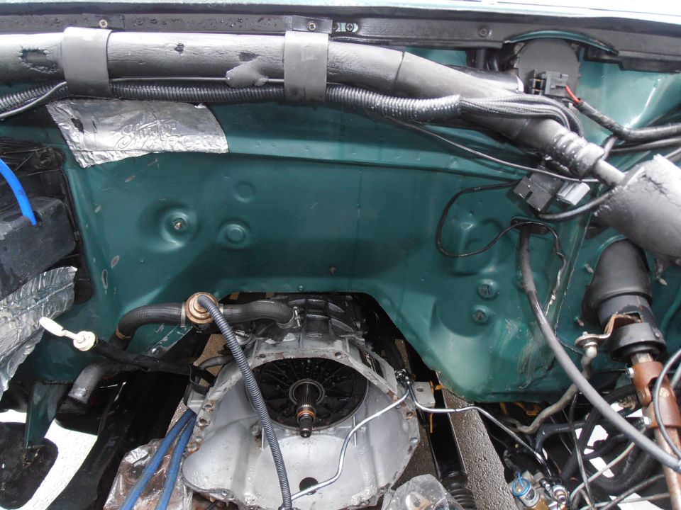 Empty green engine bay with exposed transmission bellhousing and loose wiring