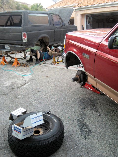 1994 Ford Bronco - Two Ford Broncos are undergoing repairs in a driveway, one being worked on by a mechanic.