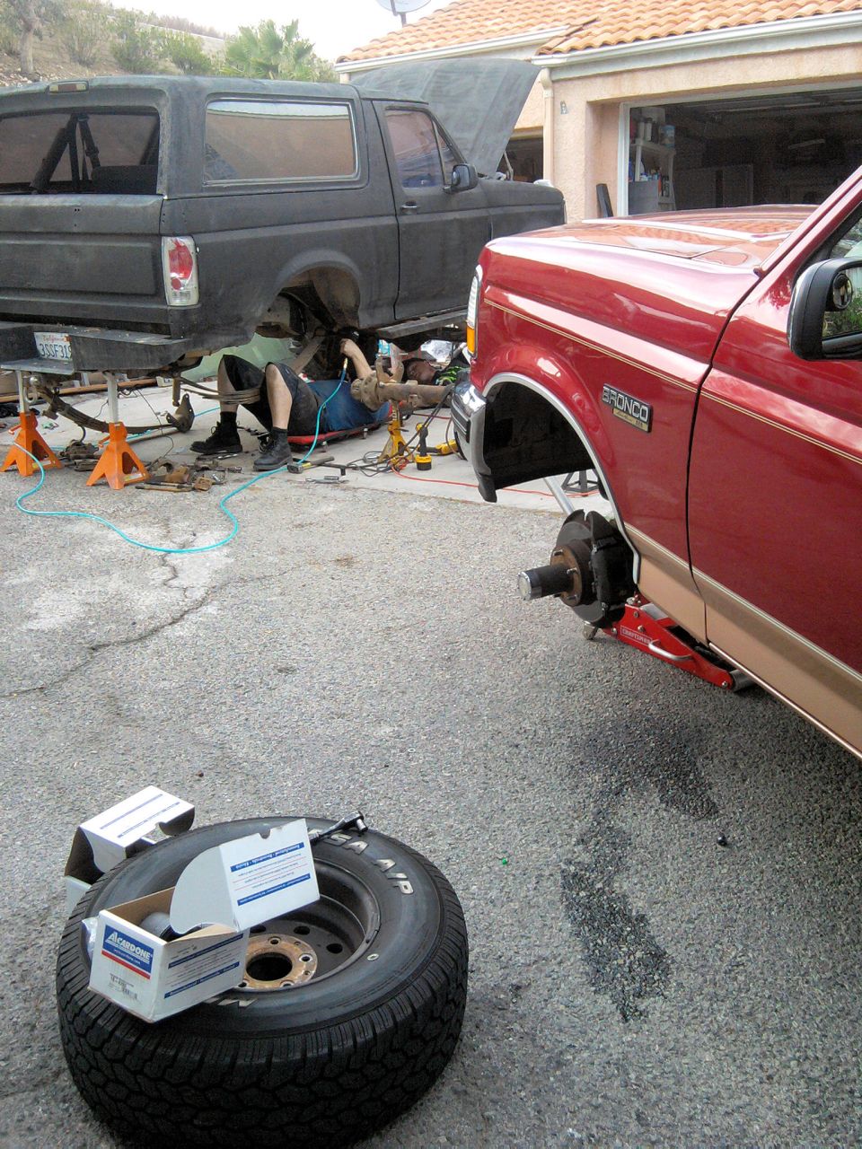 Red Ford Bronco on a floor jack with wheel removed showing bare hub, black project Bronco behind