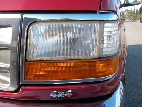 1994 Ford Bronco - Close-up of a red Ford truck's front end, showing the headlight and grille detail.