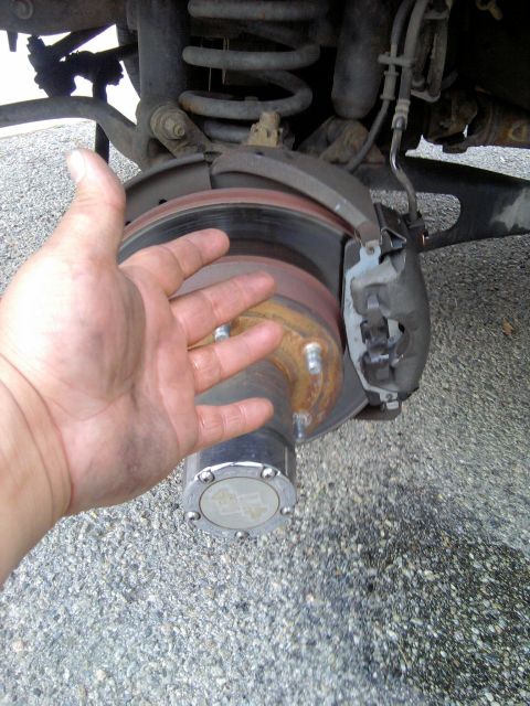 1994 Ford Bronco - Close-up of a front hub with the wheel removed, showing a rusty vented brake rotor, sliding caliper and a chrome manual locking hub cap sta…