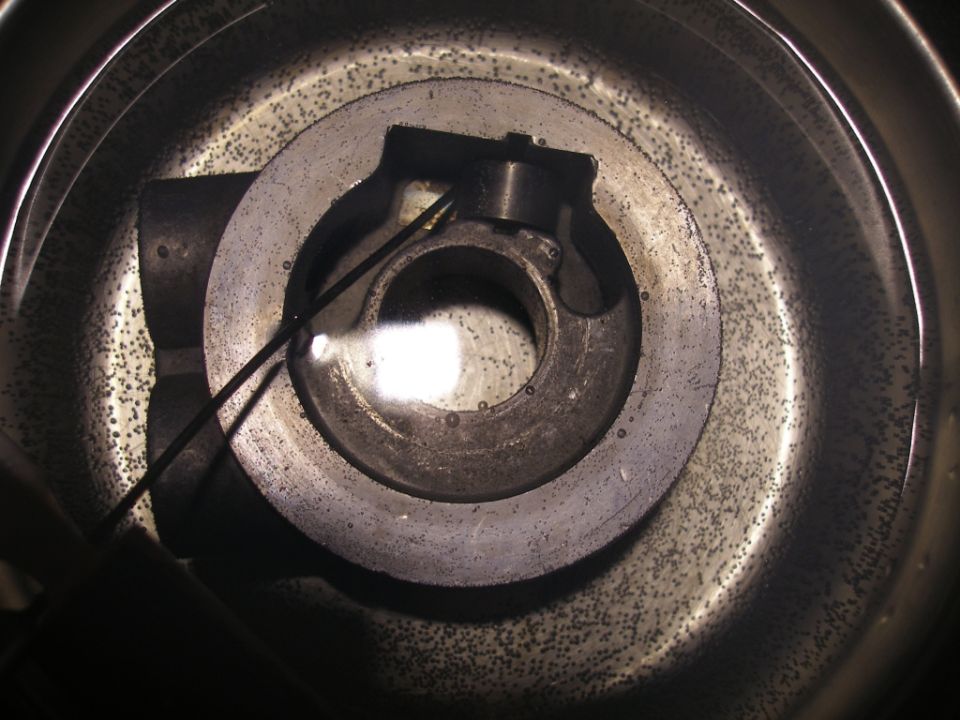 Close-up of a metal component submerged in liquid with small dark particles.
