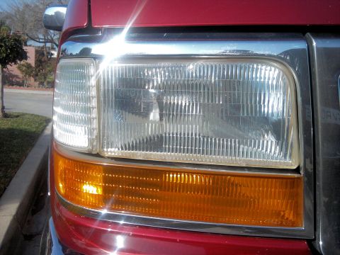 1994 Ford Bronco - The headlight and turn signal assembly on a red truck, showing the ribbed glass and chrome trim.