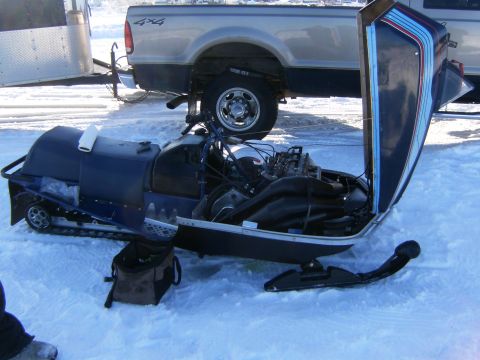 2000 Ford E350 - A snowmobile sits in the snow with its engine compartment open, revealing the internal mechanics.