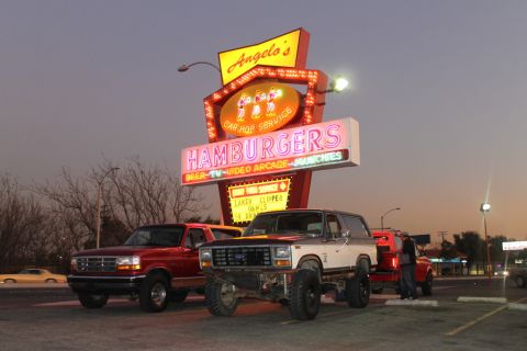 1994 Ford Bronco - Three-quarter front view of a red 1992-96 Ford Bronco parked beside a lifted red-and-white 1980-86 bullnose Bronco on chunky mud tires, bot…