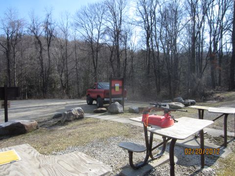 1979 Ford Bronco - A red pickup truck is parked in a wooded area next to a picnic table.
