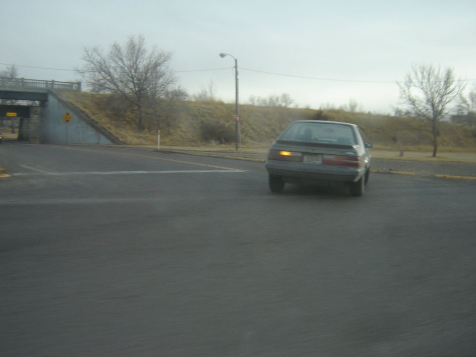 Gray Ford Mustang with yellow turn signal on, viewed from rear