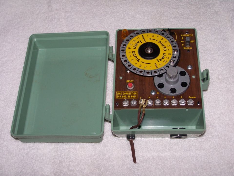 Green plastic lawn sprinkler timer with a wooden faceplate, yellow dial, and reset button