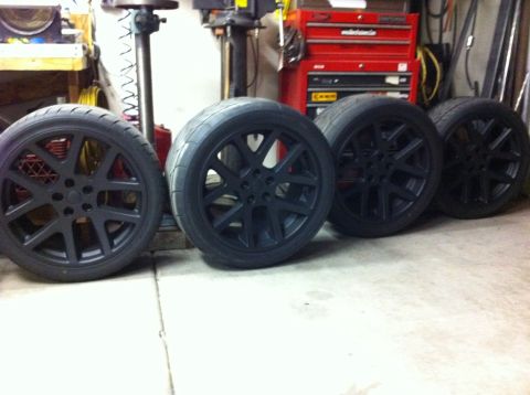 2010 Dodge Challenger - Four black wheels and tires are displayed in a garage setting, with tools visible in the background.