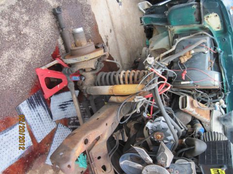 1979 Ford Bronco - Vehicle parts, including suspension and engine components, are scattered on a concrete surface.