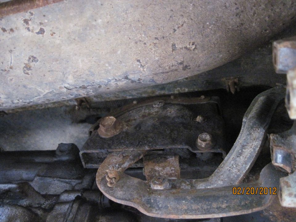Underside of a vehicle showing rusty metal brackets and pipes. Date stamp reads 02/20/2012