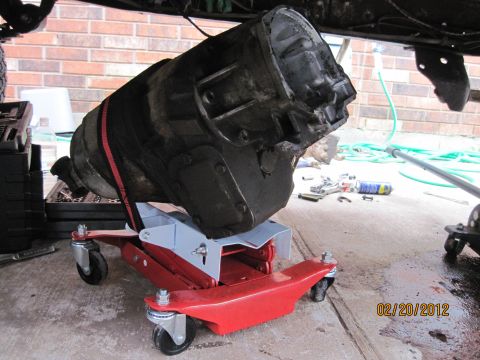 1979 Ford Bronco - A transmission is supported by a red hydraulic jack, ready for installation or removal.