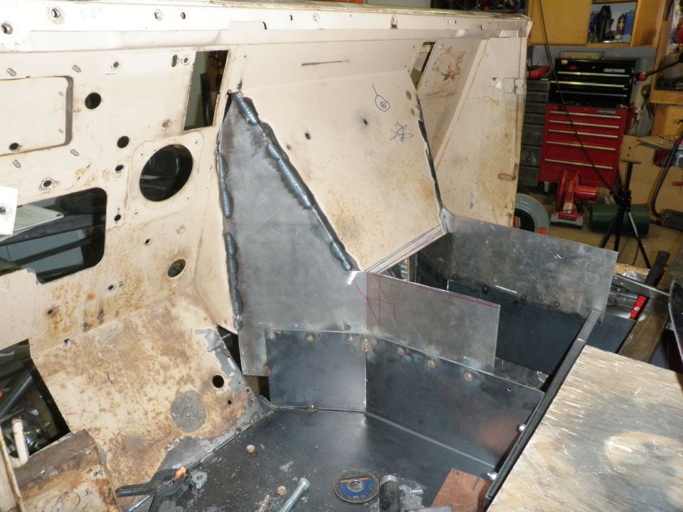 Vehicle interior with welded metal panels and exposed framework, showing rust and unfinished construction