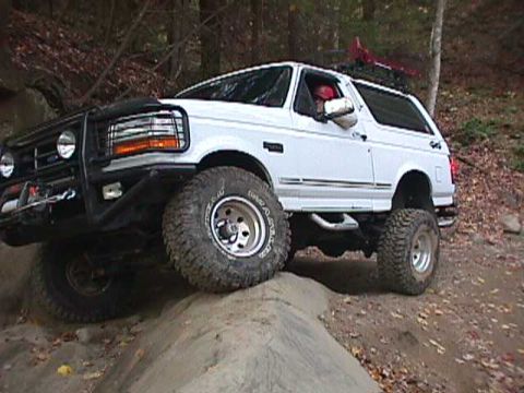 1996 Ford Bronco - White Ford Bronco navigates a rocky, wooded trail with its front tires on an incline.