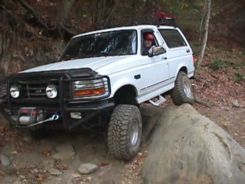 1996 Ford Bronco - A white 1996 Ford Bronco navigates a rocky trail, with its front tire high on a boulder.