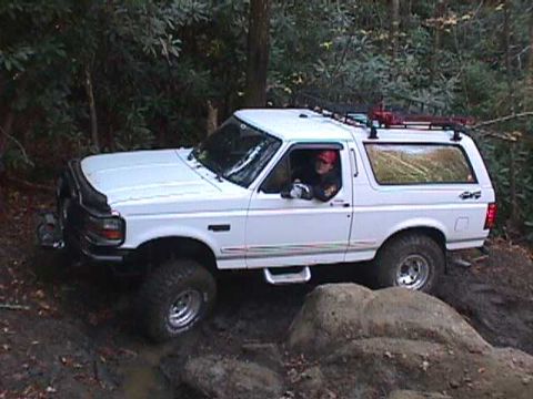 1996 Ford Bronco - White 1996 Ford Bronco navigates a rocky, off-road path in a forest.