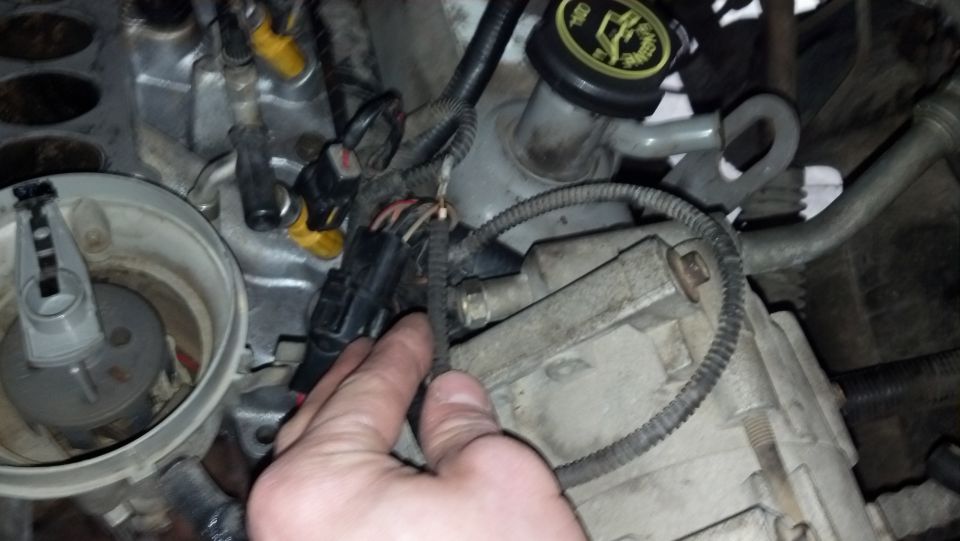 Hand holding a black wiring connector with cut wires in a Bronco engine bay near the distributor